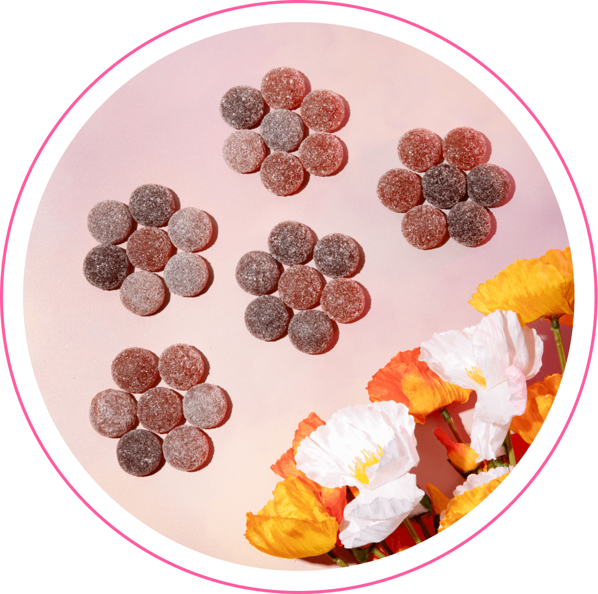 Gumdrop candies arranged in flower-like clusters on a pink background with white and orange poppy flowers at lower right.